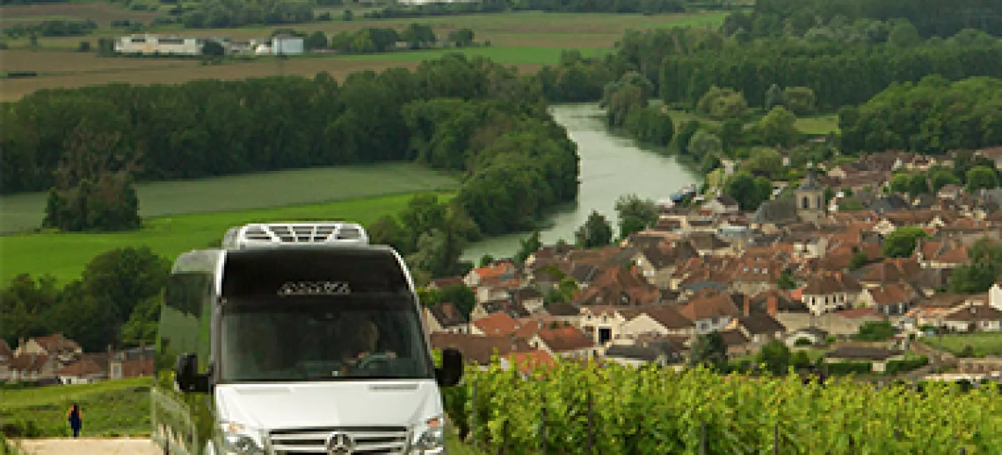 Mini coach driving through a vineyard near a village in a European wine region.