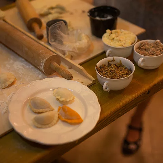 A plate of pierogis resting next to a rolling pin and other kitchen implements.